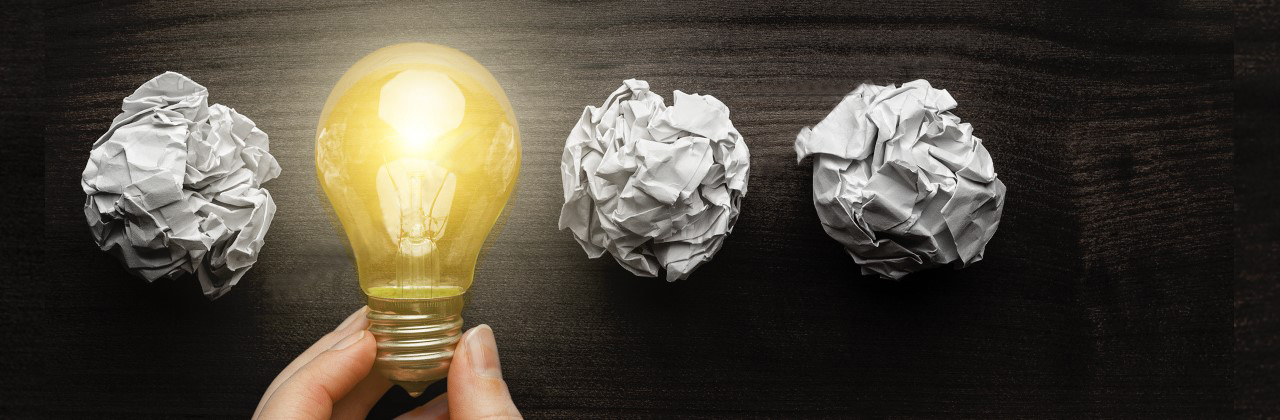 A lightbulb turned on with three rolled up balls of paper: one on the left and two on the right on a black background