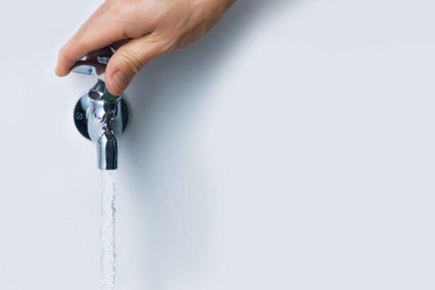 This image is a hand turning on a water spigot and water flowing out the spout. 