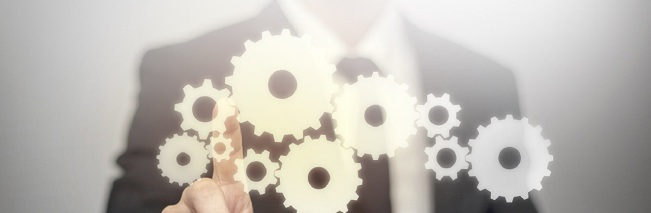A suited man pointing up towards a bunch of machine cogs