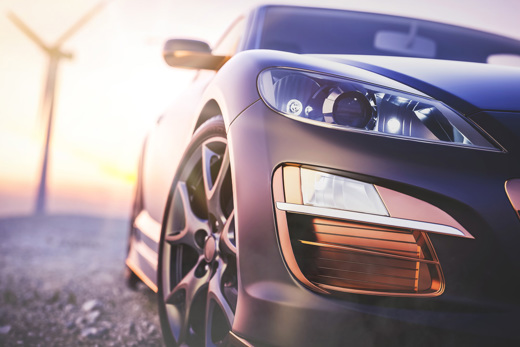 Parked electric car with wind mill in background.
