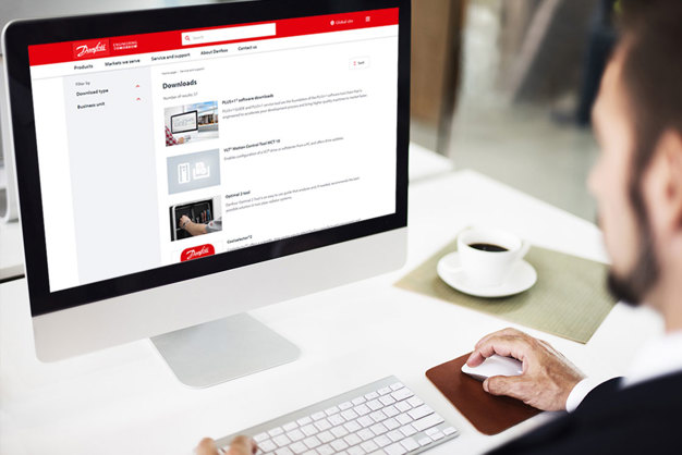 A bearded gentleman looking at a non-branded Apple computer, using the Danfoss.com website while drinking a cup of coffee