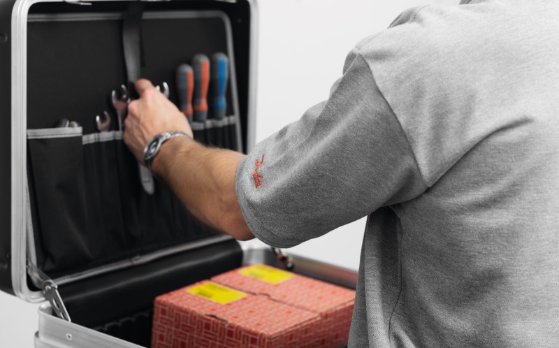 An HVACR technician in a grey Danfoss shirt grabbing tools from a kit that holds Danfoss aftermarket products inside.