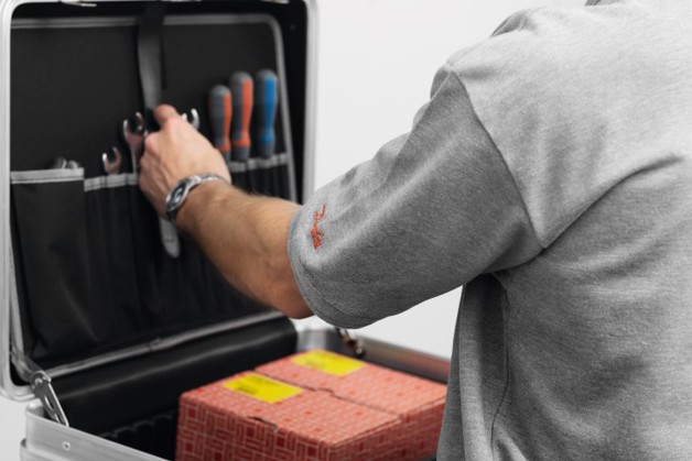 An HVACR technician in a grey Danfoss shirt grabbing tools from a kit that holds Danfoss aftermarket products inside.