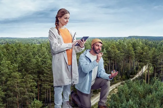 A man and a woman looking at a tablet in forest