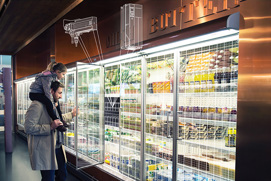 Man with his daughter on his shoulders, looking into a refrigeration case at a supermarket