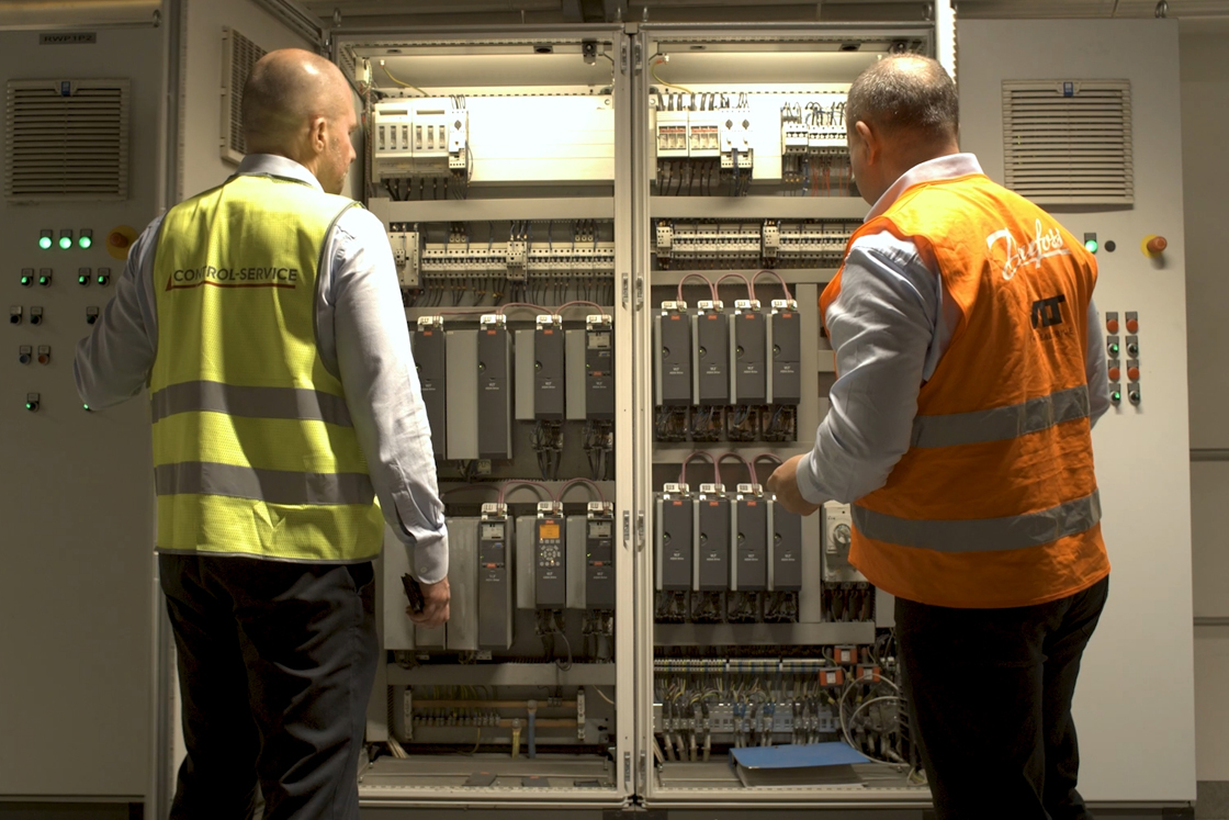 2 men looking at VLT drives in a cabinet