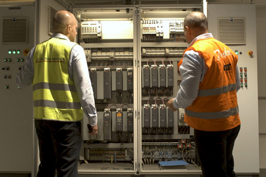 2 men looking at VLT drives in a cabinet